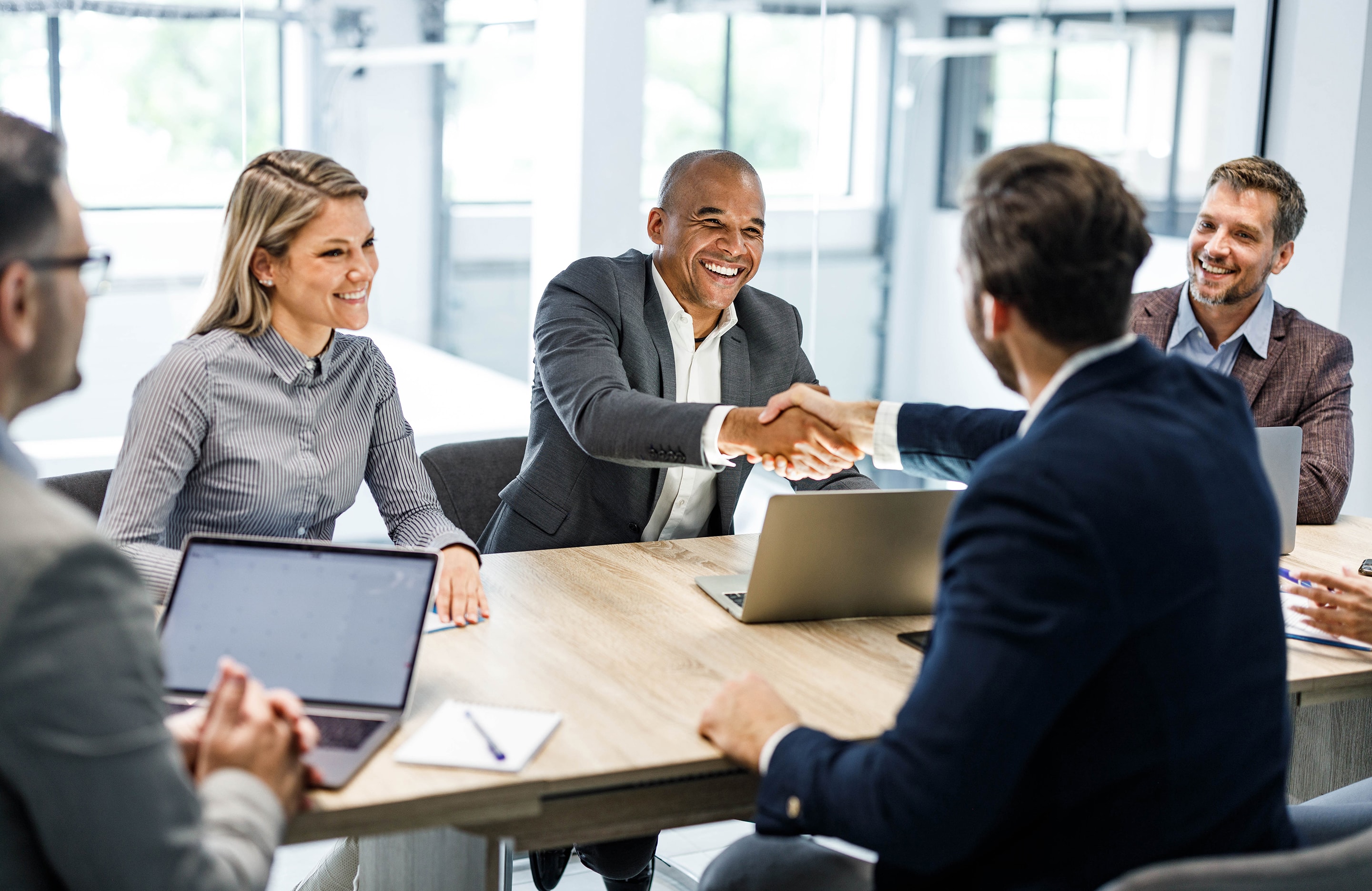 Employer extending job offer with others at a table in an office