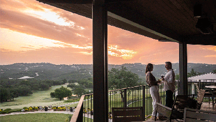 man and woman couple standing on balcony enjoying a glass of wine at sunset