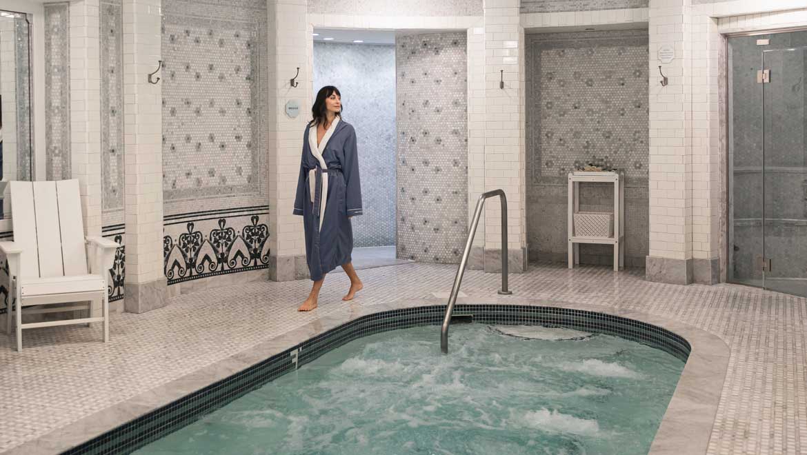 Woman in spa robe walking near hot tub.